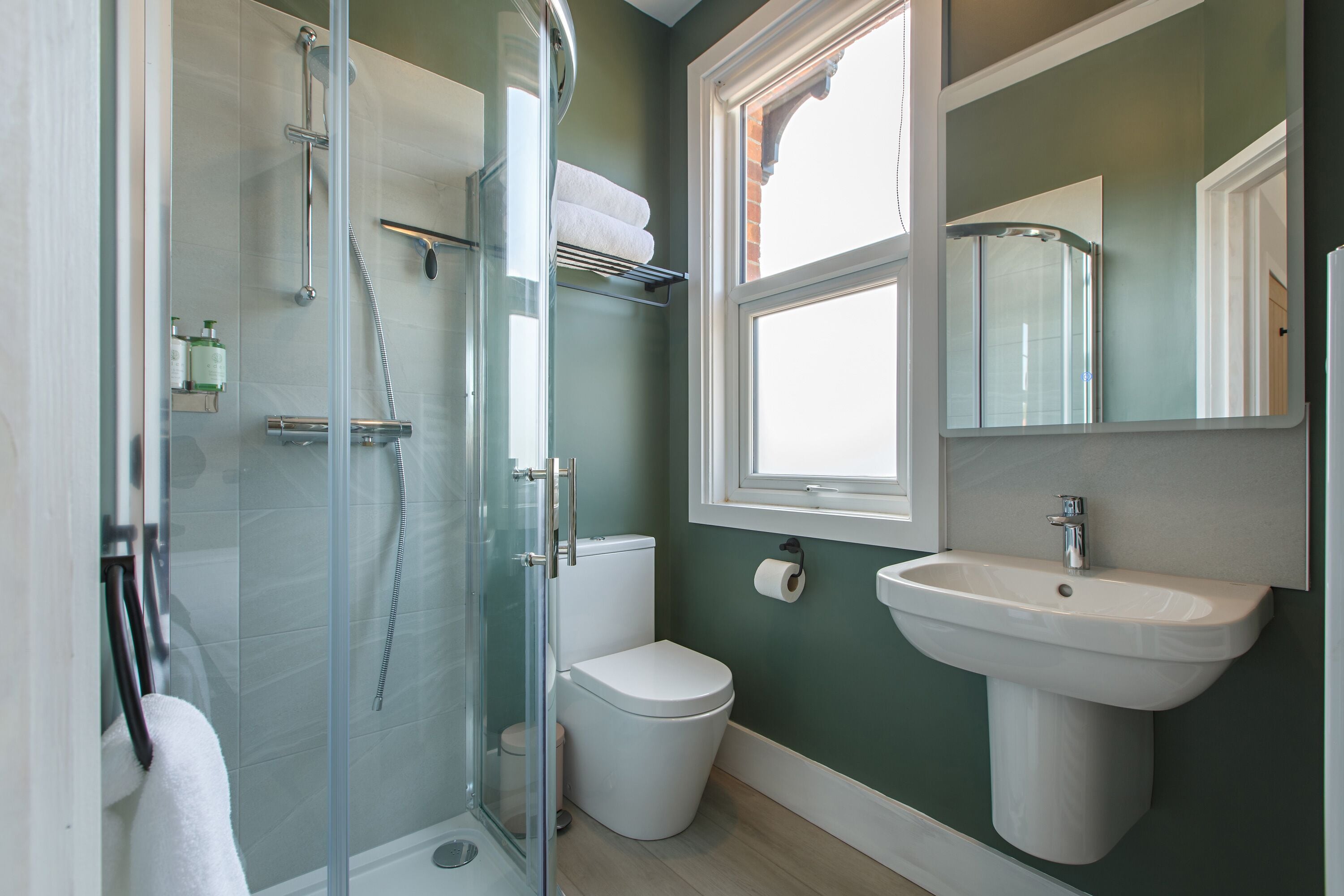 Un baño moderno con ducha envuelta en cristal, inodoro blanco y lavamanos sobre pedestal.