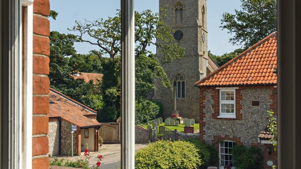 A view of a church with a clock tower, surrounded by brick buildings and greenery. - The Ship Inn (Holt)