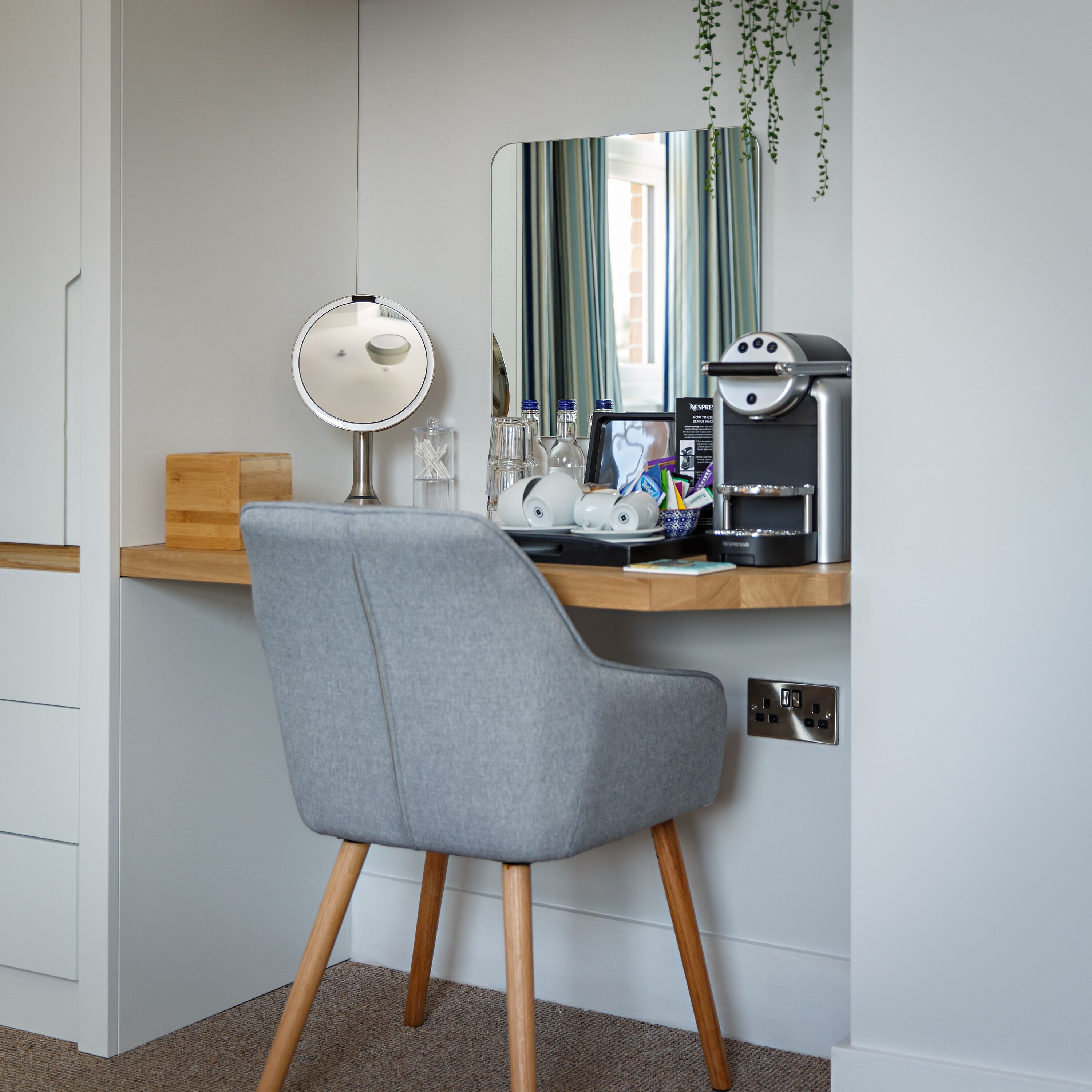 Un espace de travail moderne avec une chaise grise, un miroir rond, une machine à café et une étagère en bois.