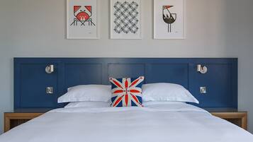 A neatly made bed with white linens, a blue headboard, and a Union Jack pillow.