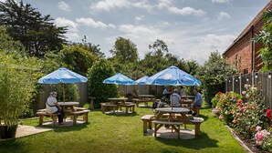 An outdoor patio area with picnic tables and blue umbrellas. - The Ship Inn (Holt)