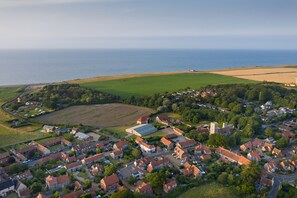 An aerial view of a coastal village with houses, a church, and a large open field.