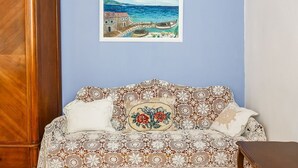 A room with a wooden wardrobe, a patterned sofa with floral cushions, and a framed painting of a coastal scene. - Villa Lyubov - Three Bedroom Villa, Sleeps 9 (Tisno)