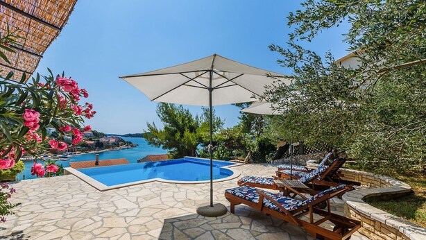 A poolside area with a stone patio, lounge chairs, and umbrellas. - Villa Lyubov - Three Bedroom Villa, Sleeps 9 (Tisno)