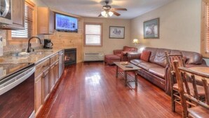 A spacious living area with a fireplace, leather sofa, and a television mounted on the wall. - Gone Fishing: Secluded Cabin in Woods Overlooking Beautiful Mountain Stream (Gatlinburg)