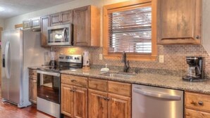 A kitchen with wooden cabinets, stainless steel appliances, a brick backsplash, and a window with blinds. - Gone Fishing: Secluded Cabin in Woods Overlooking Beautiful Mountain Stream (Gatlinburg)