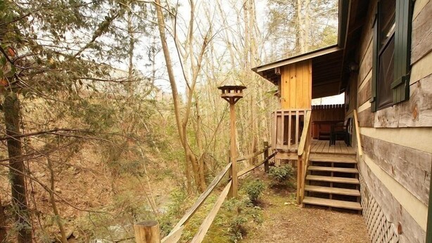 A wooden cabin with a wooden staircase leading to a deck, surrounded by trees and a stream. - Gone Fishing: Secluded Cabin in Woods Overlooking Beautiful Mountain Stream (Gatlinburg)