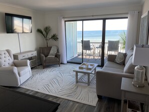 Relax in a comfortable living space with a sofa, armchairs, and a flat-screen TV, plus a sliding door to an ocean-view balcony.