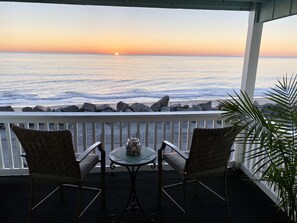Enjoy the ocean view from this seaside balcony with a wicker chair and small table.