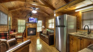 Ein Ferienhaus-Innenraum mit Holzvertäfelung, einem Kamin, einer Couch, einem Fernseher und einem Kühlschrank.