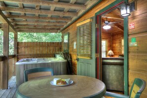 Une cabane en bois avec un bain à remous, une table sur laquelle se trouve une assiette de nourriture et une porte donnant sur un coin cuisine.