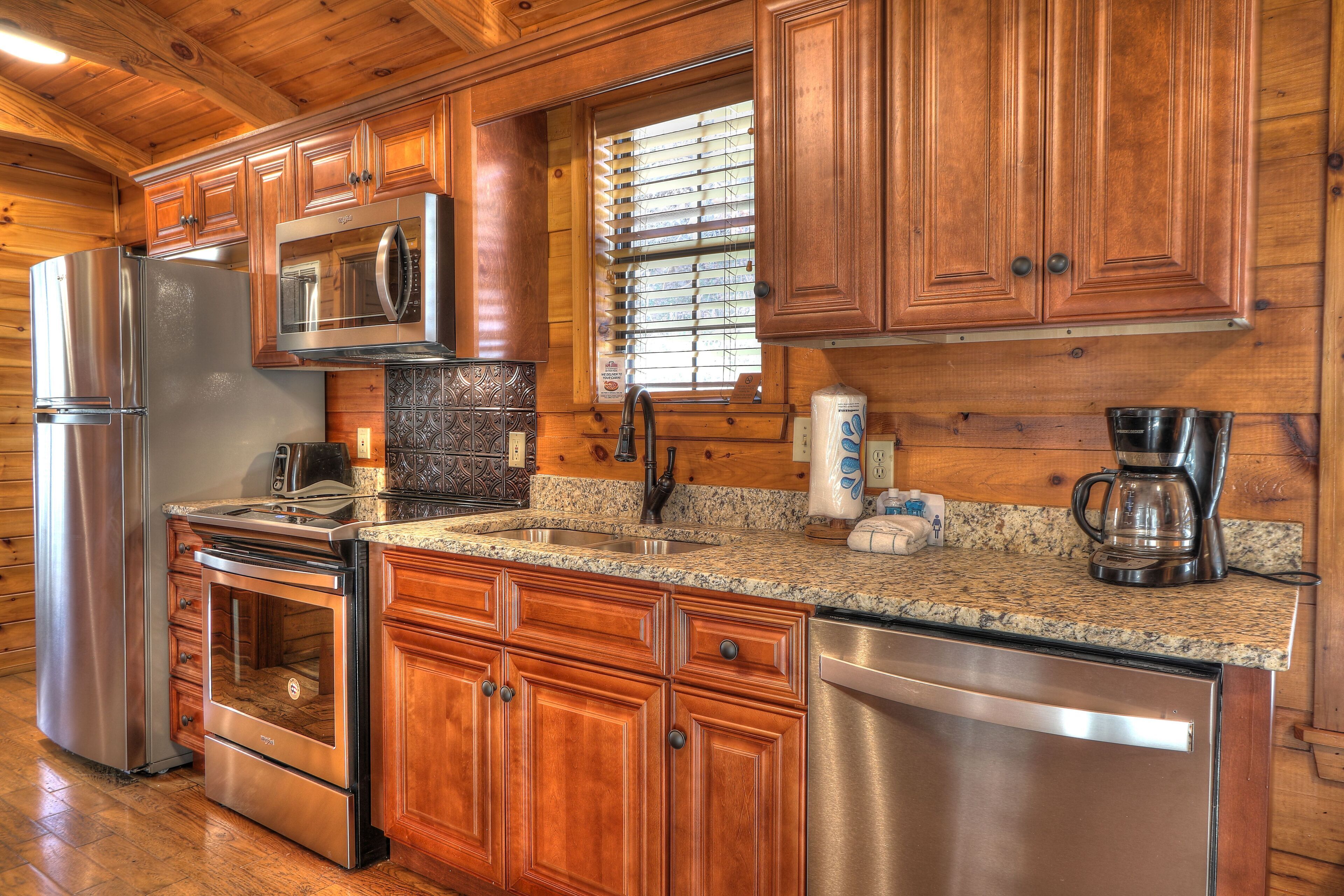 A kitchen with wooden cabinets, stainless steel appliances, granite countertops, and a window with blinds.