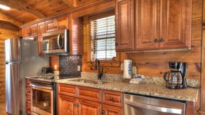 A kitchen with wooden cabinets, stainless steel appliances, granite countertops, and a window with blinds. - Oakview: Pet-Friendly Cabin Nestled in a Secluded Wooded Area Only Minutes from Downtown Gatlinburg (Gatlinburg)