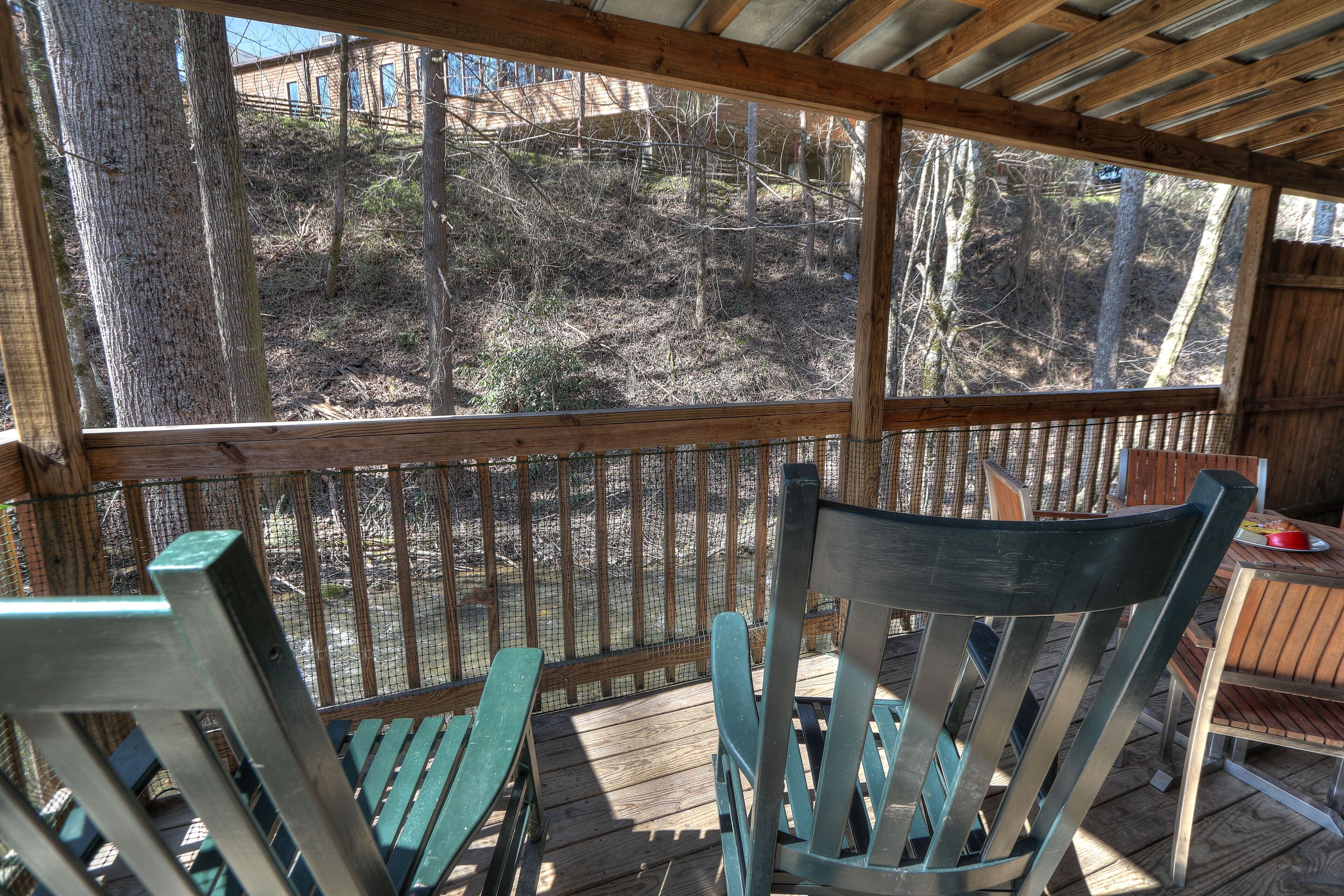 A wooden deck with a view of a wooded area, a table with chairs, and a fenced enclosure.