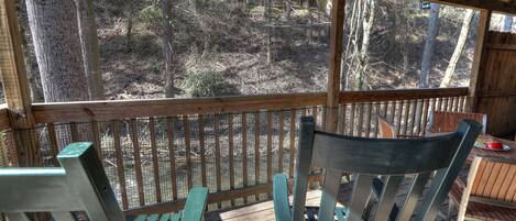 A wooden deck with a view of a wooded area, a table with chairs, and a fenced enclosure.