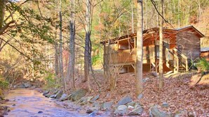 A cabin with a wooden deck and stairs leading to a porch, surrounded by trees and a stream. - Oakview: Pet-Friendly Cabin Nestled in a Secluded Wooded Area Only Minutes from Downtown Gatlinburg (Gatlinburg)