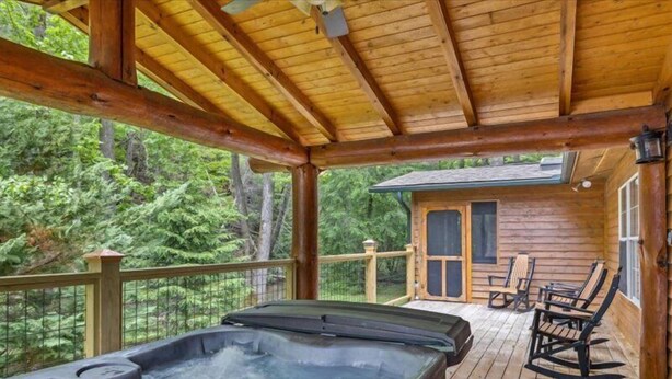 Une terrasse en bois avec un jacuzzi, des sièges d’extérieur et un chalet en arrière-plan.