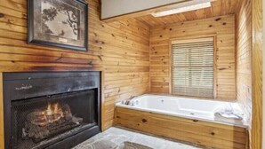 L’intérieur d’un chalet en bois, avec une cheminée en pierre, un tableau encadré et une grande baignoire.