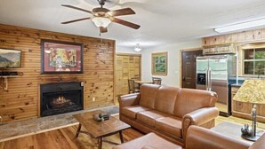 Un salon doté d’une cheminée, de murs en bois, d’un ventilateur de plafond et d’un coin repas.