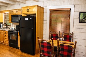 Een keuken met houten kasten, een zwarte koelkast en een eettafel met geruit stoelen.