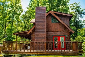 Een houten chalet met een rode deur en een balkon.