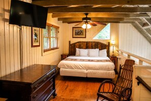 A bedroom with a bed, wooden headboard, a ceiling fan, a dresser, a chair, and a TV mounted on the wall.