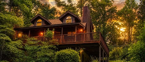 A two-story wooden cabin with a balcony, surrounded by dense greenery.