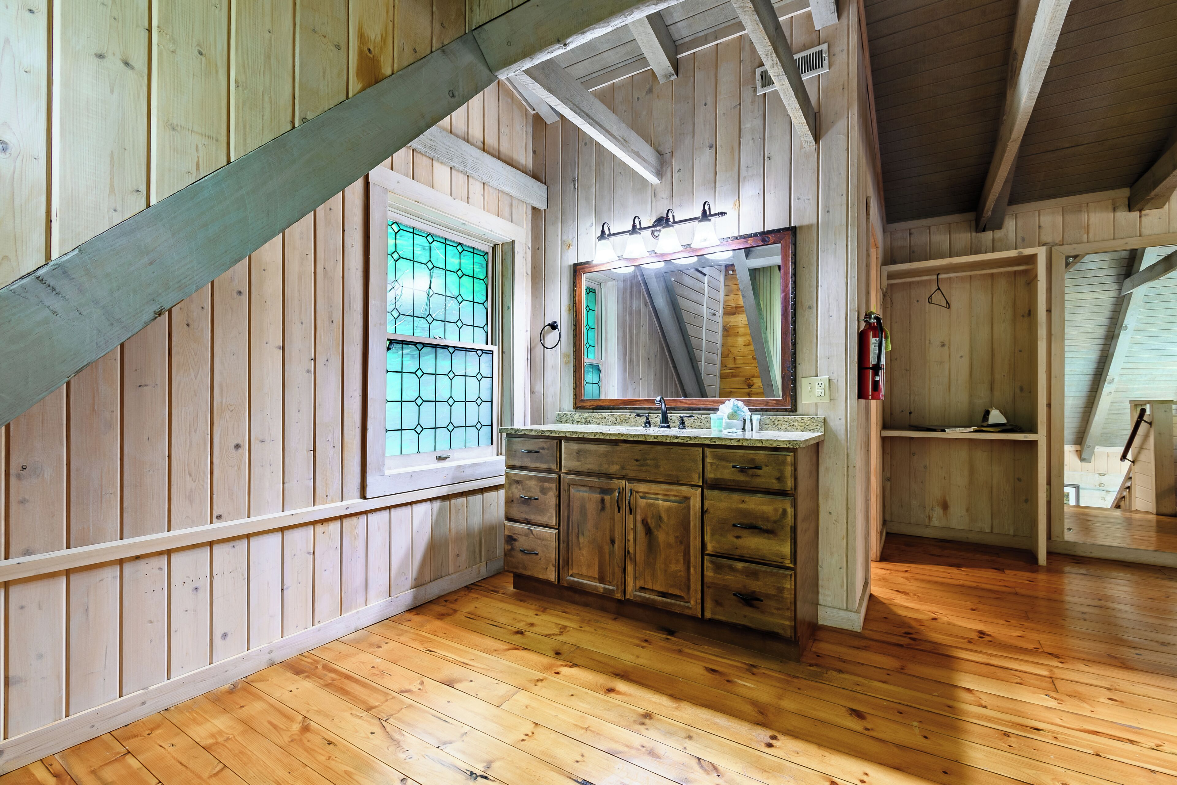 A wooden interior with a kitchen area, wooden walls, and a sloped ceiling.