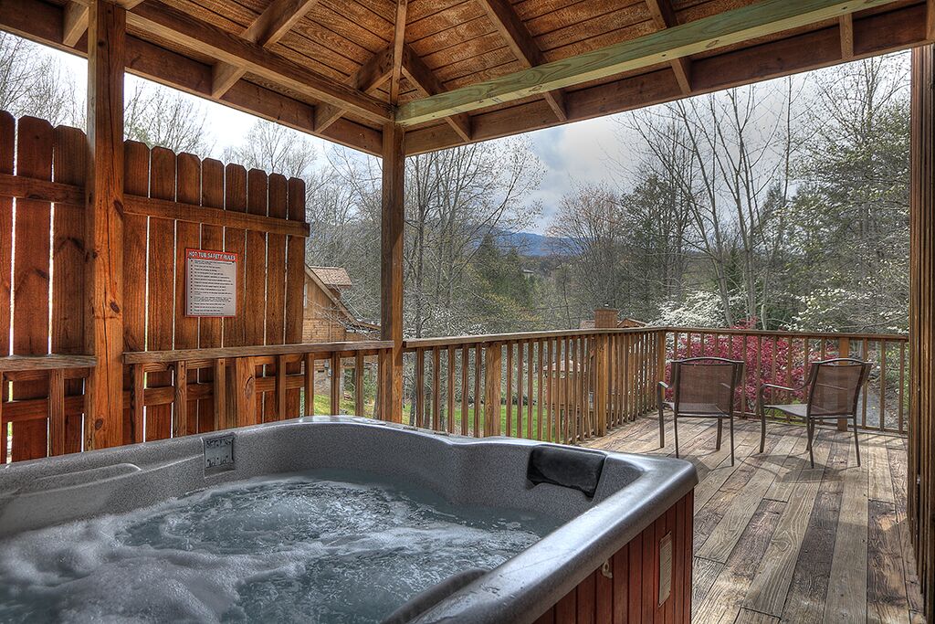 Un jacuzzi en una terraza de madera con valla y sillas.