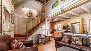 Un interior de cabaña acogedor, con una escalera de madera, sofás de cuero, un comedor y una cocina con electrodomésticos modernos.