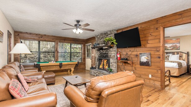 A cozy living room with a pool table, leather sofas, a fireplace, and a television mounted on the wall.
