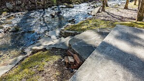 A concrete pathway leading to a small stream in a forested area with rocks and moss.