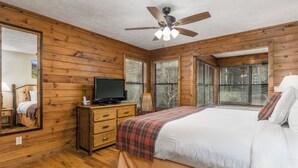 A wooden-paneled bedroom with a bed, a television on a dresser, and a ceiling fan.