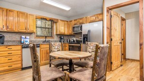 A kitchen with wooden cabinets, a stainless steel refrigerator, a microwave, and a dining table with chairs.