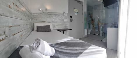 Een moderne hotelkamer met een groot bed, een klein nachtkastje, een airconditioner en een glazen deur naar een badkamer.