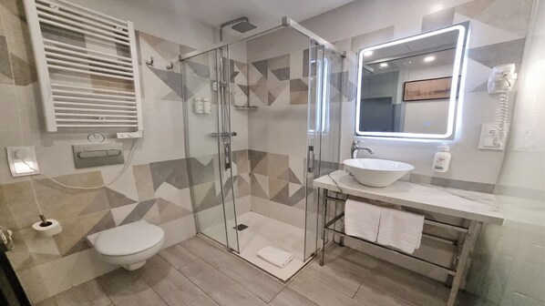 Een moderne badkamer met een douche met glazen wand, een witte wastafel en een badkamermeubel met spiegel.