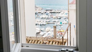 A view from a window overlooking a marina with boats docked, a mountainous backdrop, and a building with a red roof. - Hotel Clopy Rocamar (Benidorm)