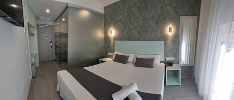 Una habitación de hotel moderna con una cama grande, una mesita de noche, un armario empotrado y un baño con cabina de ducha de vidrio.