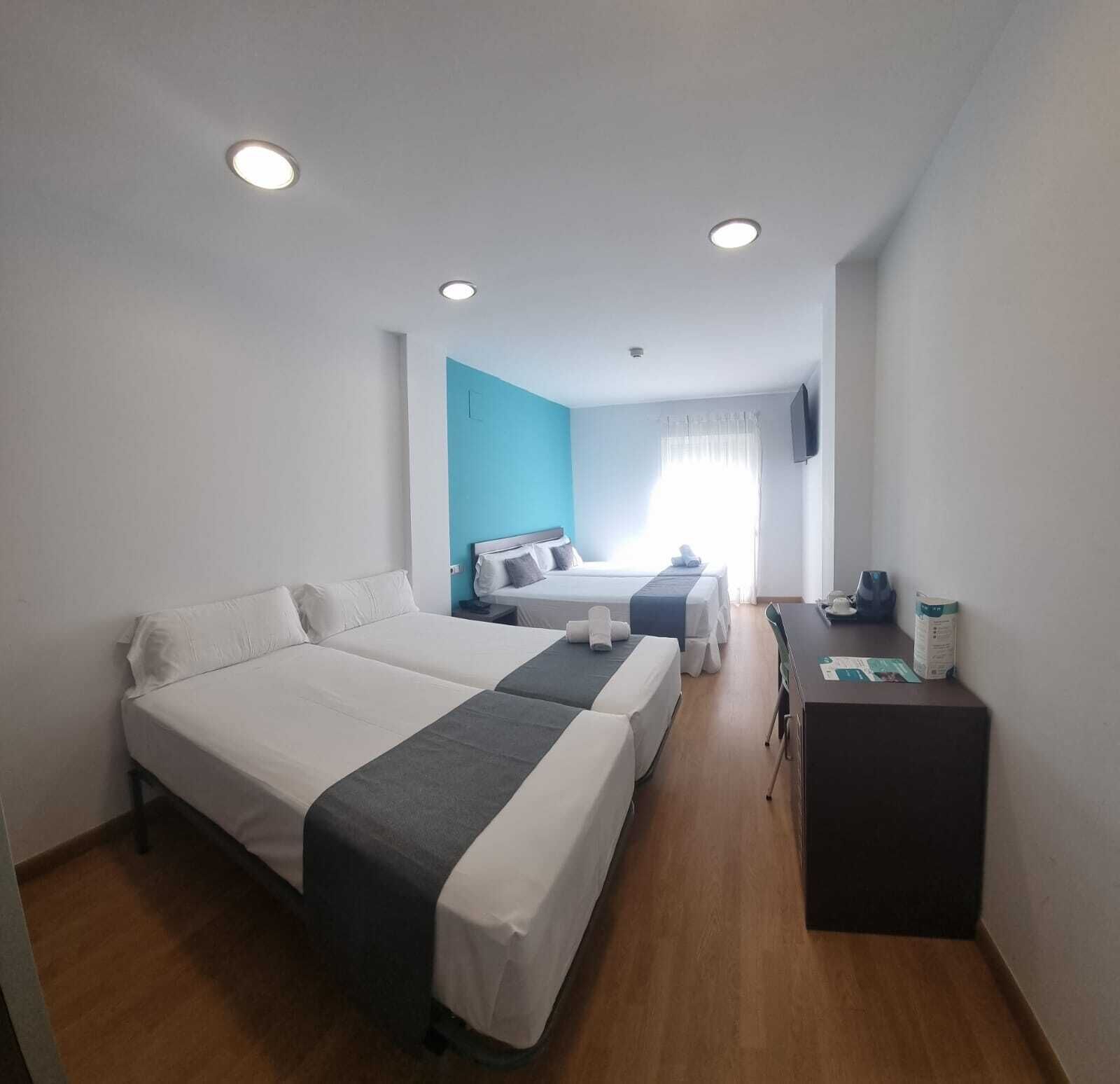 A hotel room with two beds, a desk, a TV, and a window with curtains.