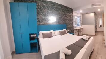 Habitació d'hotel moderna amb un llit gran, un armari blau, un escriptori petit i un bany amb rentaplat i mirall.