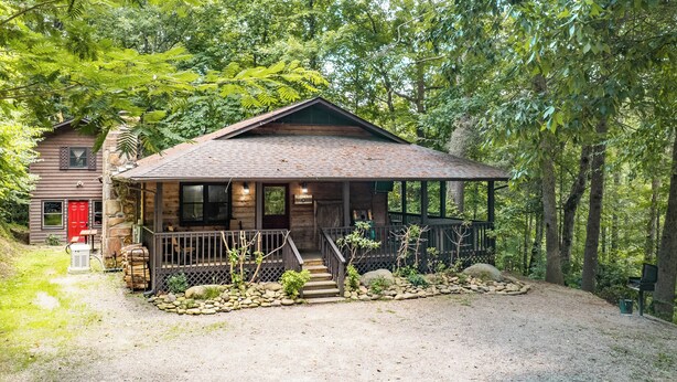 A rustic cabin with a stone foundation, a wooden porch, and a gravel driveway. - Wildflower Haven: Beautiful Secluded Cabin in Gatlinburg, Just Minutes from Downtown Gatlinburg. (Sevierville)