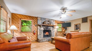 A cozy living room with a stone fireplace, leather sofas, wooden flooring, and a ceiling fan. - Wildflower Haven: Beautiful Secluded Cabin in Gatlinburg, Just Minutes from Downtown Gatlinburg. (Sevierville)