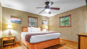 A bedroom with a bed, two bedside tables with lamps, a ceiling fan, and wooden flooring. - Wildflower Haven: Beautiful Secluded Cabin in Gatlinburg, Just Minutes from Downtown Gatlinburg. (Sevierville)