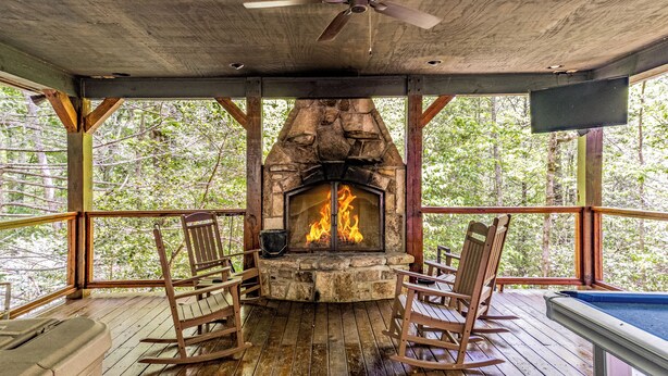 Ein überdachter Außenbereich mit Kamin aus Stein, Holzstühlen und einem Billardtisch.