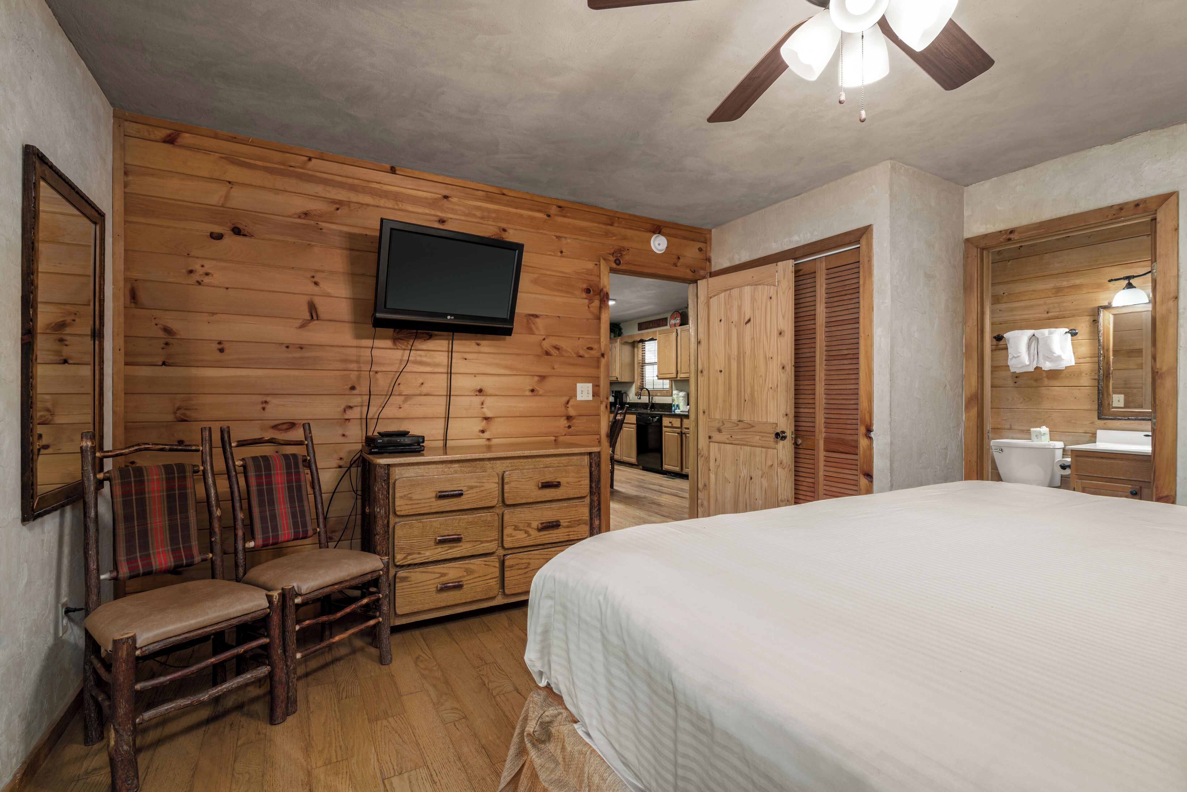 Een slaapkamer met houten lambrisering, een bed, een televisie, een houten dressoir en een stoel.