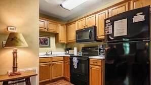 A kitchen with wooden cabinets, a black refrigerator, a microwave, and a stove. - Cub's Den: Beautifully Located, Cozy Cabin Surrounded by The Great Smoky Mountains (Gatlinburg)