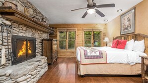 Una camera da letto con camino in pietra, pareti in legno, un letto con copriletto e una ventola a soffitto.