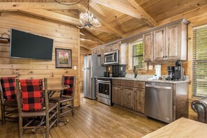 Enjoy cooking and dining in this fully equipped kitchen with a large flat-screen TV, stainless steel appliances, and a dining area with a wooden table.