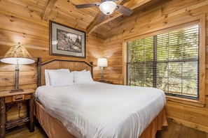 Cozy retreat with a large bed, bedside tables, and a ceiling fan, featuring a framed picture above the bed and a window with blinds.