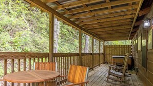 A wooden deck with a table and chairs, surrounded by a wooden fence, overlooking a forested area.